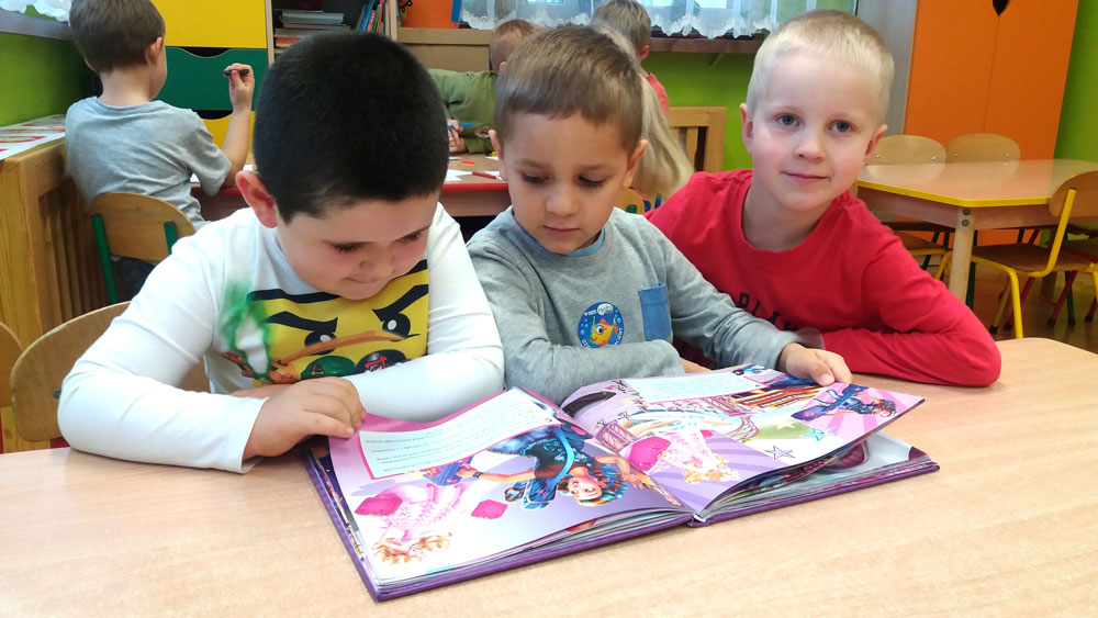 Zdjęcie trzech chłopców w bibliotece przy książce